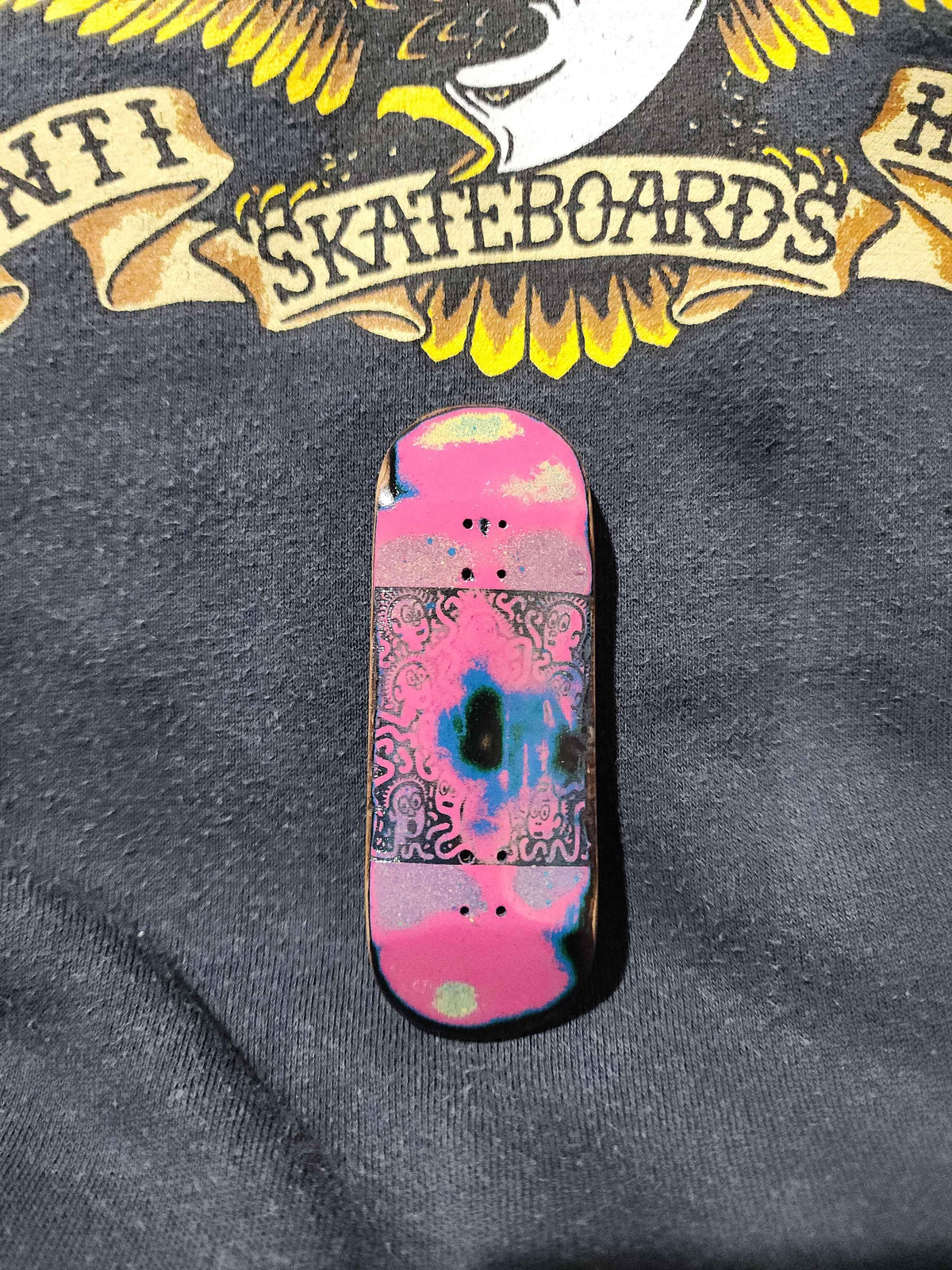 Custom pink and blue patterned fingerboard deck on a black graphic t-shirt
