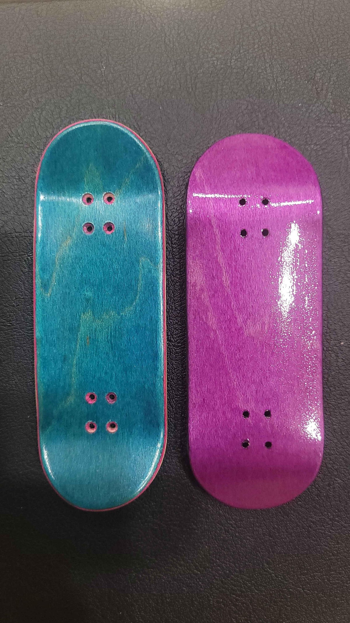 Two handmade custom fingerboard decks in teal and purple wood finishes.