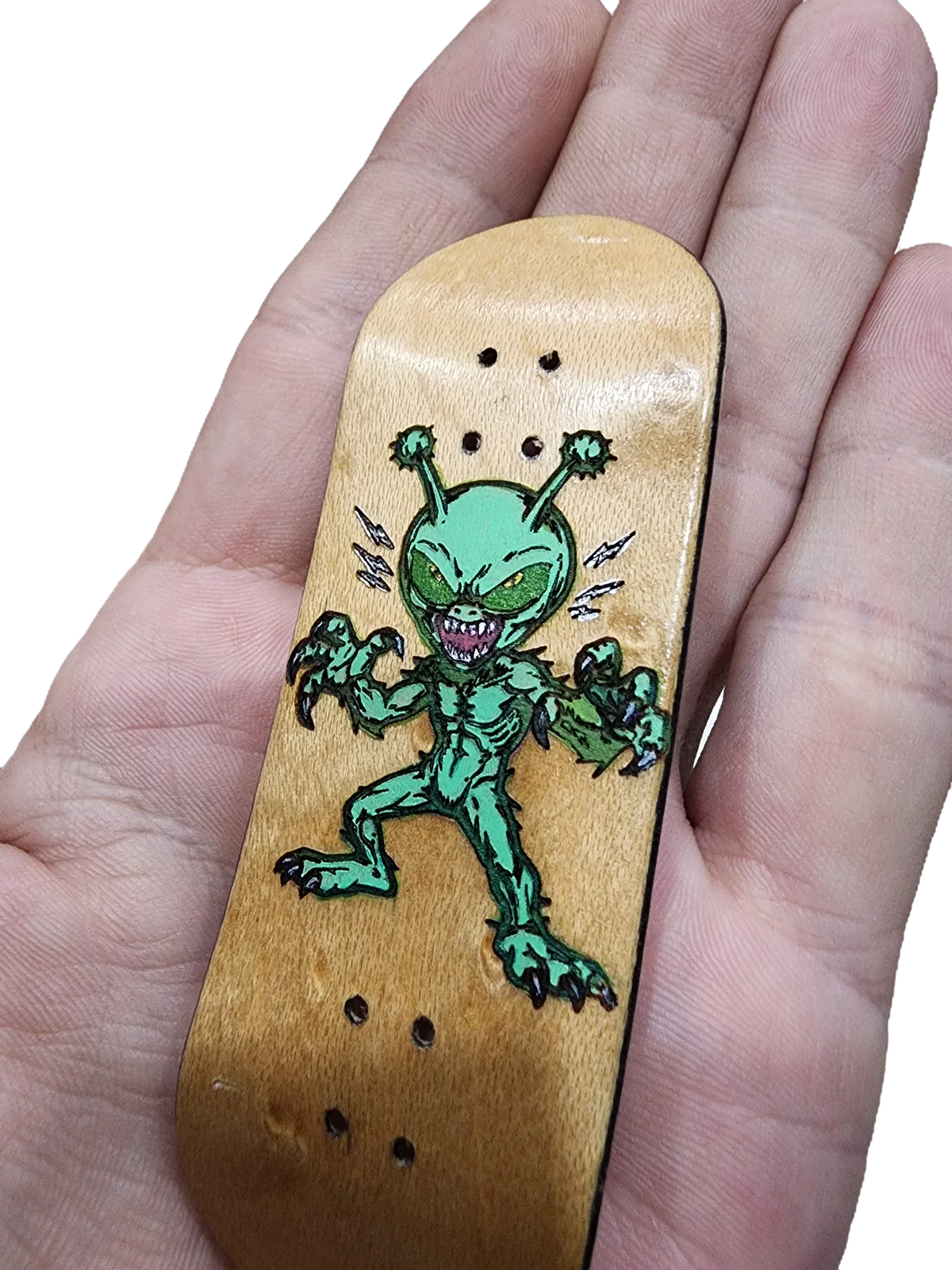 Hand holding a wooden fingerboard deck featuring a green alien graphic.