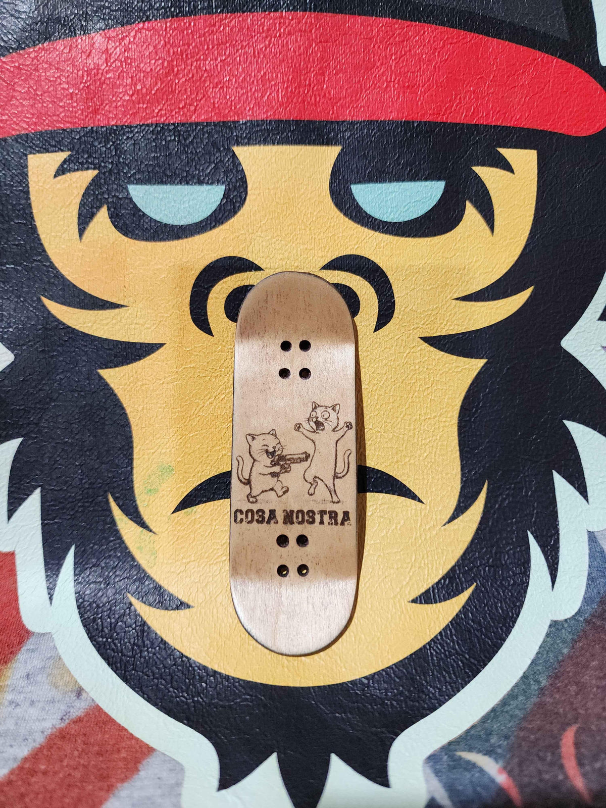 Cosa Nostra wooden fingerboard deck with cat graphics on a stylized lion background