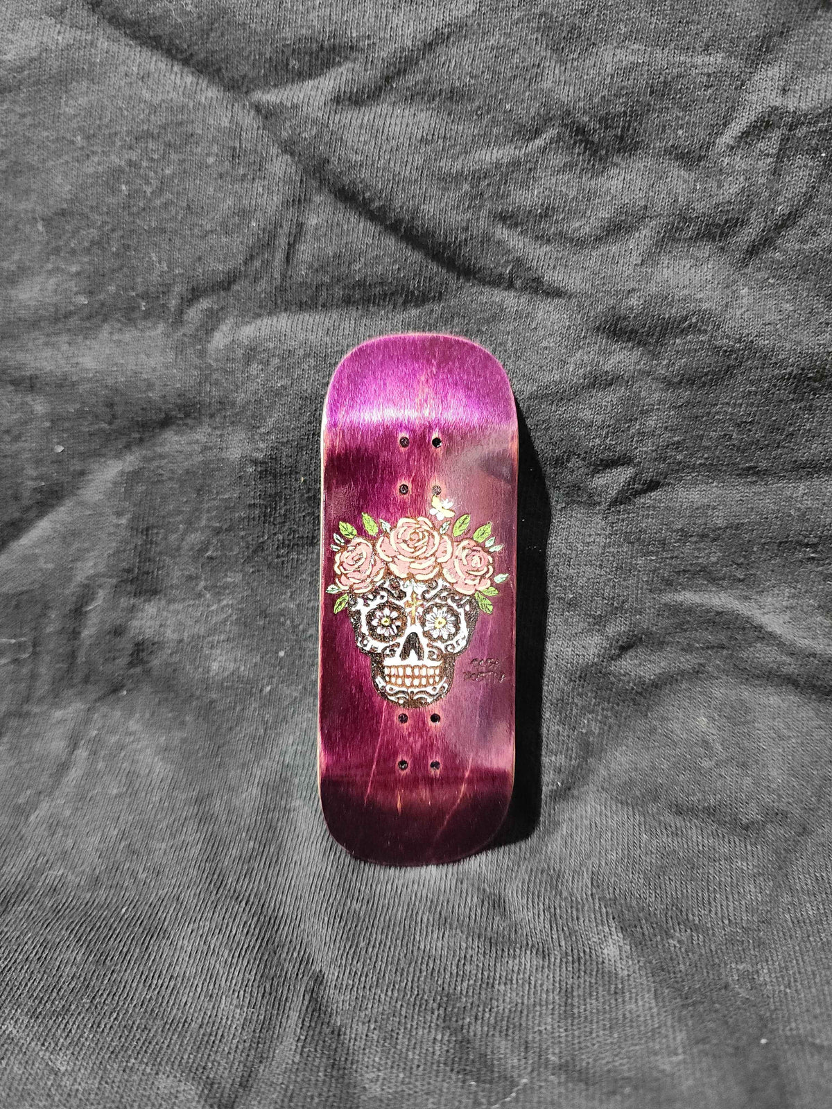 Handmade purple fingerboard deck with sugar skull and rose graphic design.