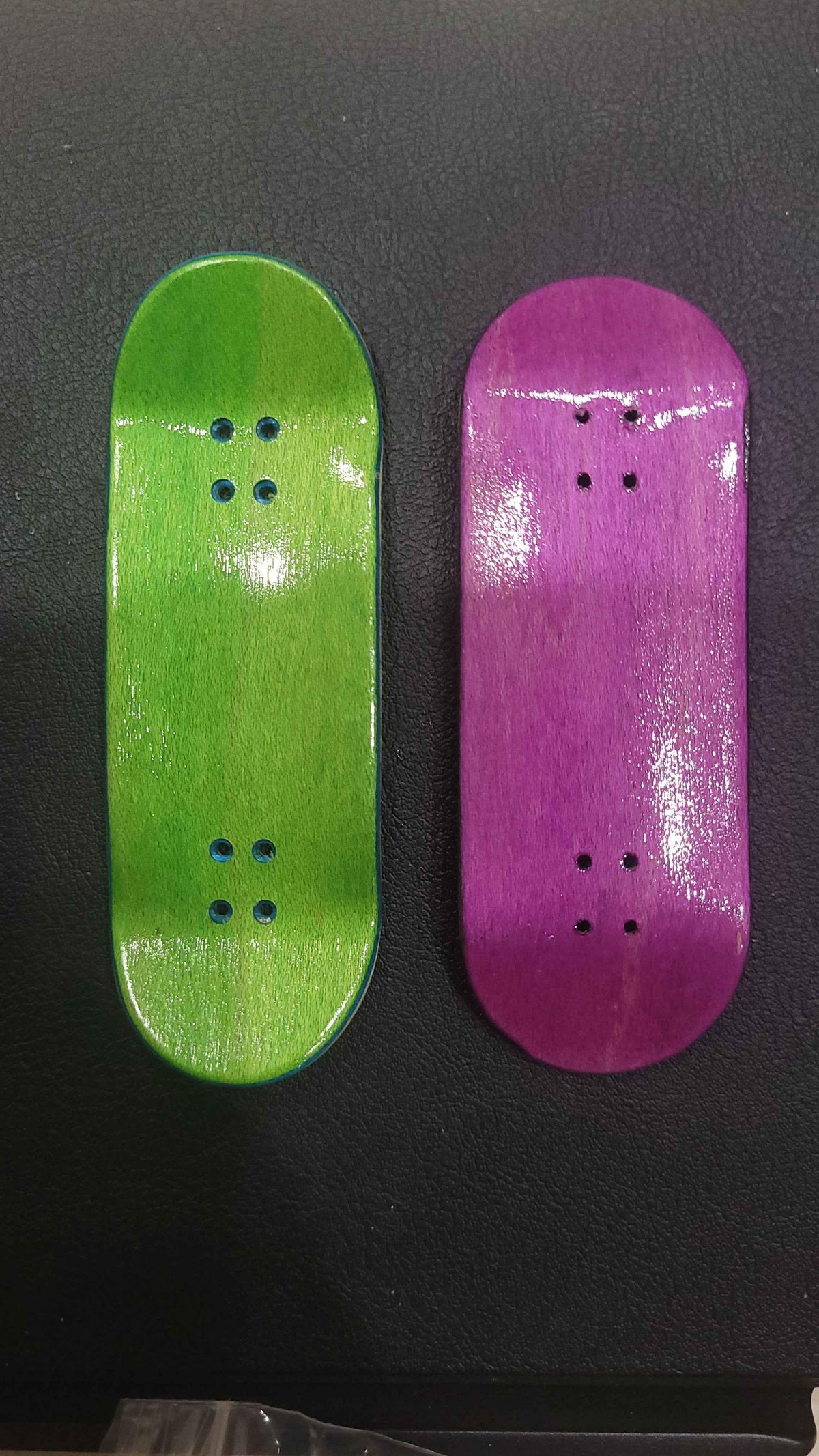 Two handmade custom fingerboard decks in lime green and purple wood finishes.