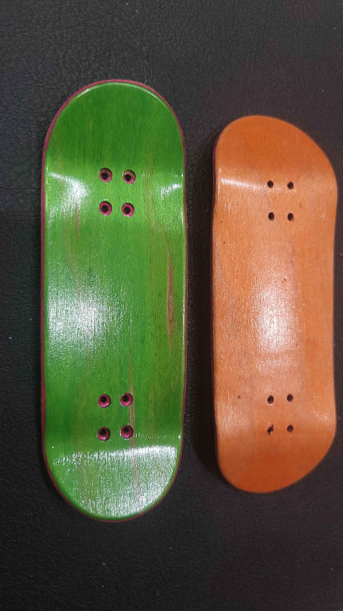 Handmade green and orange wooden fingerboard decks on a black surface.