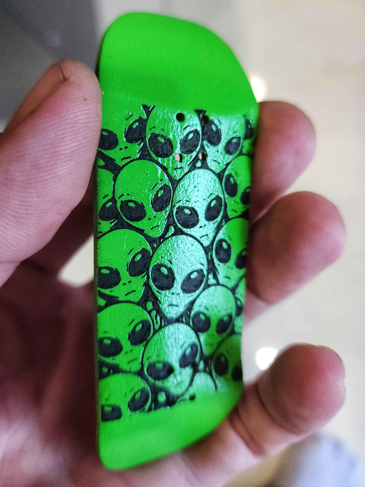 Custom neon green fingerboard deck with black alien head graphic pattern.
