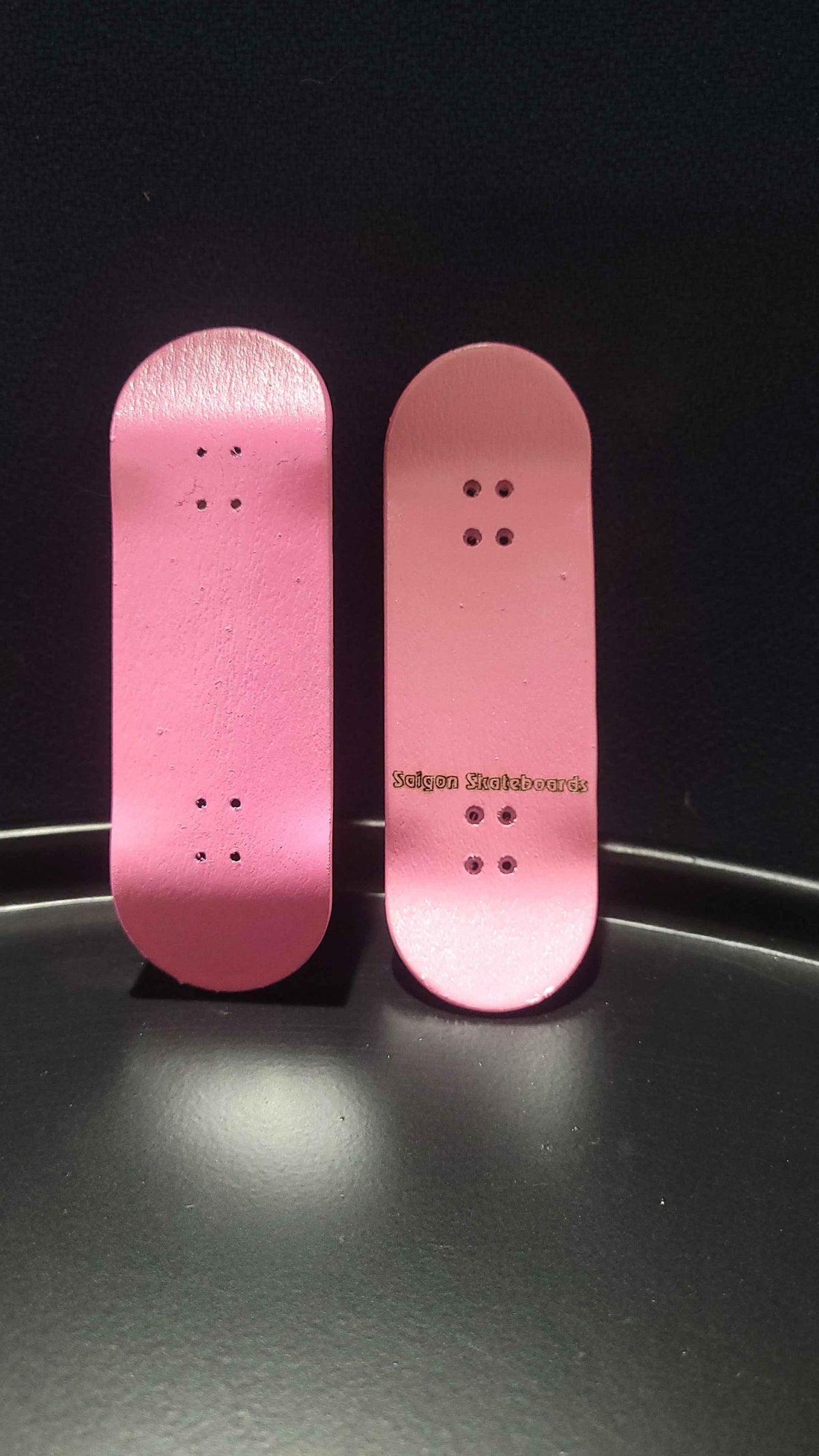 Two pink handmade custom fingerboard decks on a black surface.