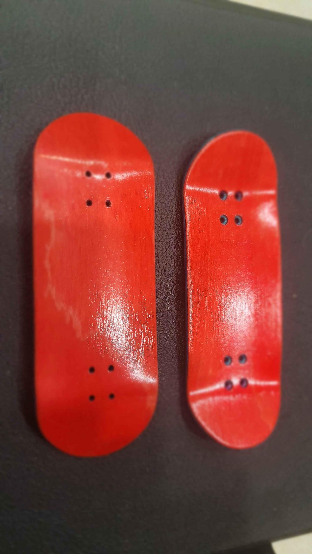 Two handmade red wooden fingerboard decks on a black surface.