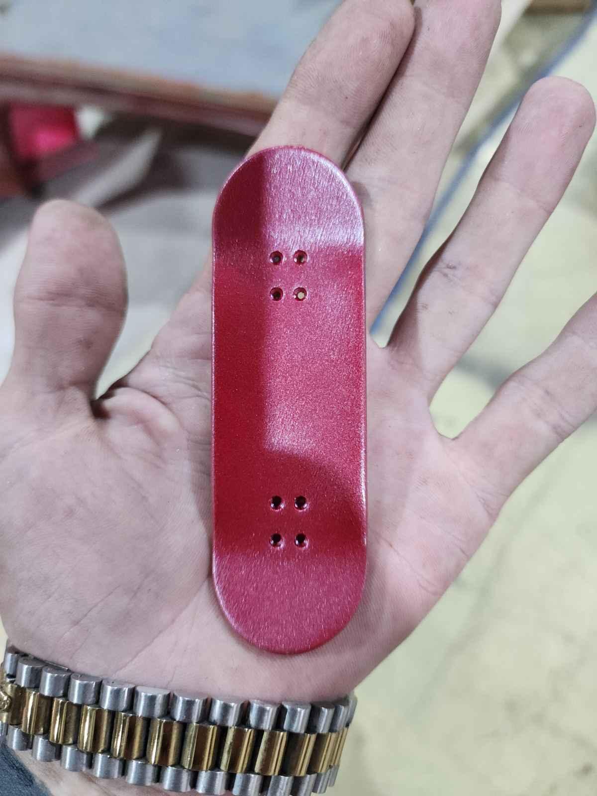 Hand holding a custom red handmade fingerboard deck.