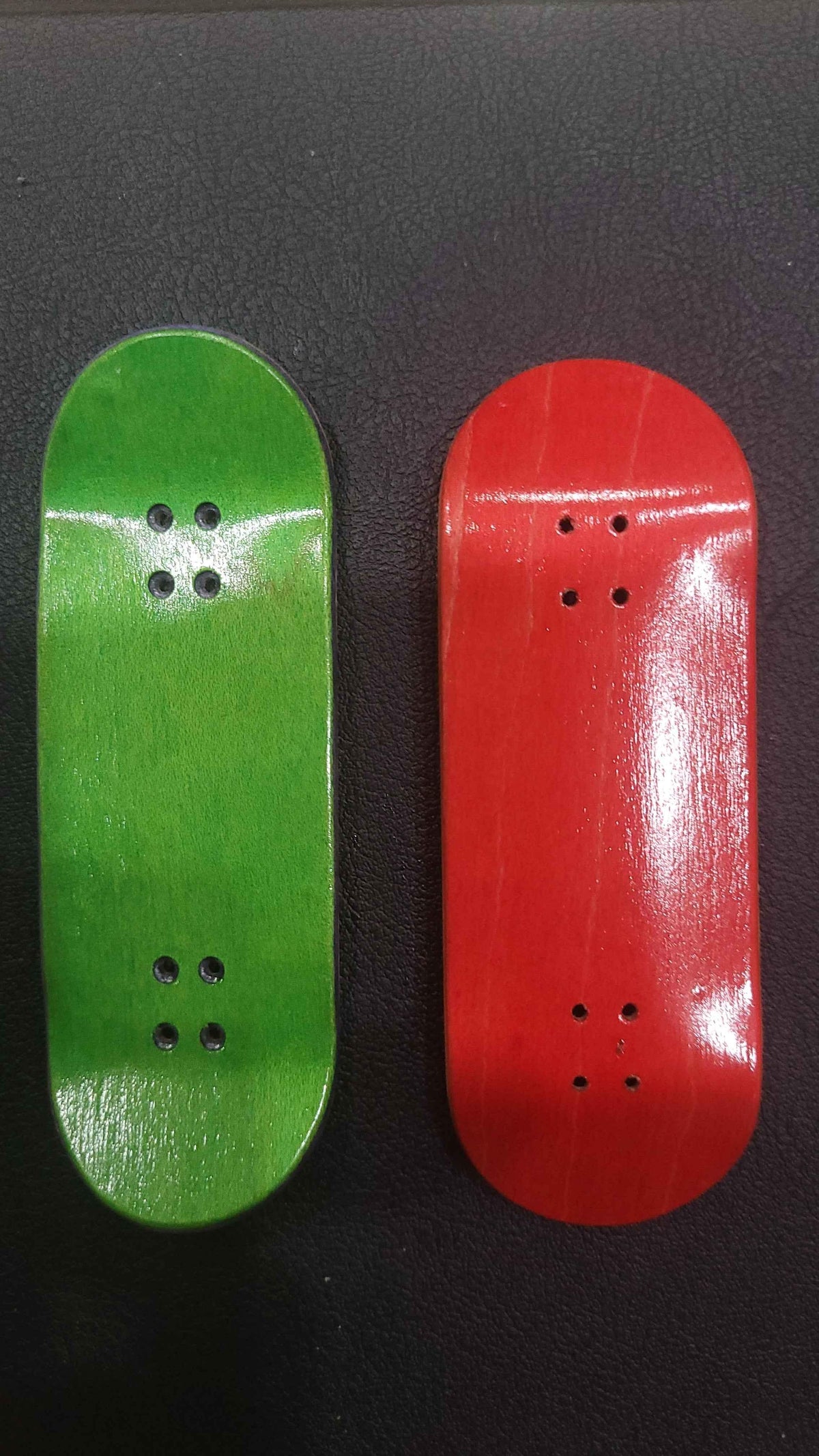 Handmade green and red custom fingerboard decks on a dark surface.