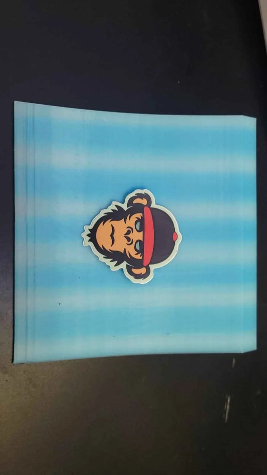 Cartoon monkey head sticker with a red cap on a light blue striped background.
