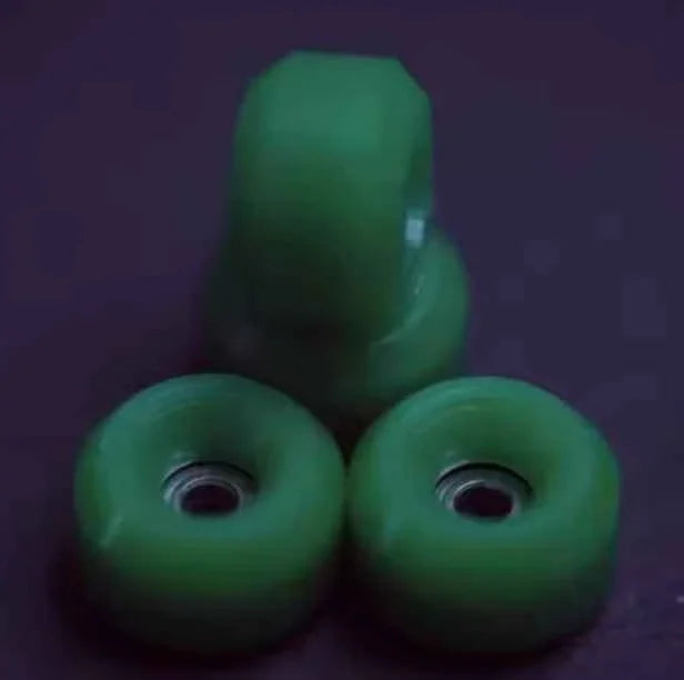 Three small, translucent green fingerboard wheels stacked on a dark purple background.