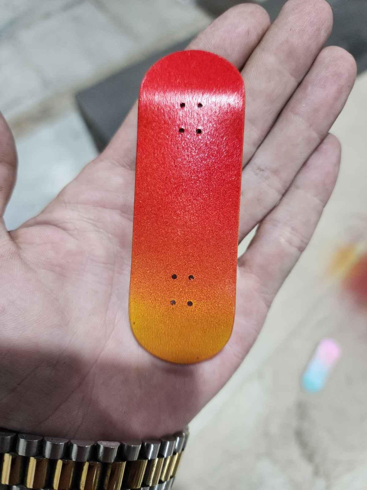 Handmade red and orange gradient custom fingerboard deck held in a hand.