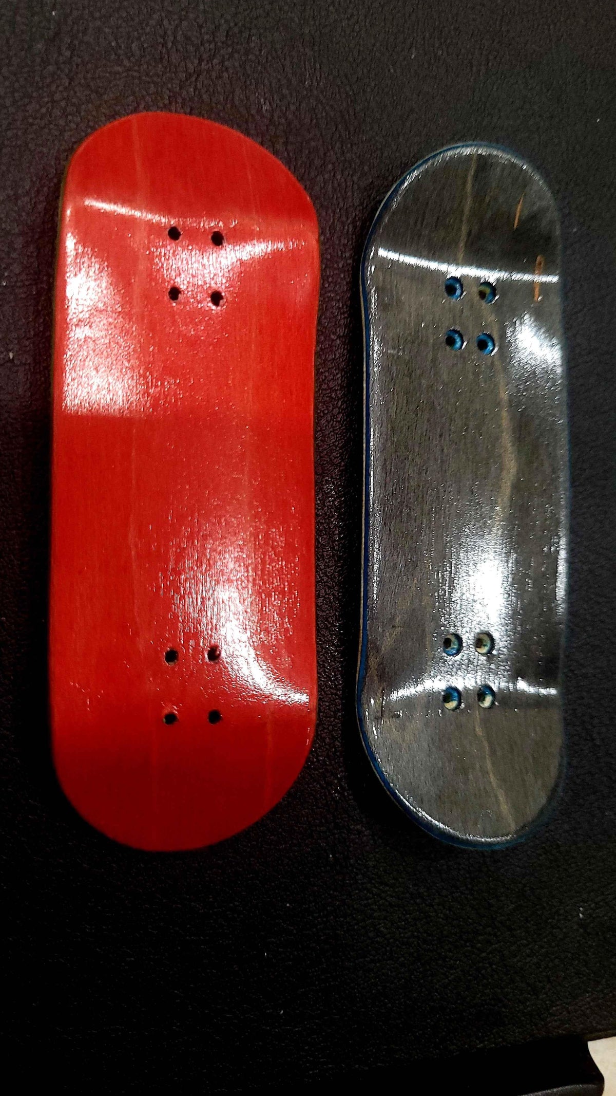 Two custom handmade fingerboard decks, one red and one natural wood finish, on a dark surface.