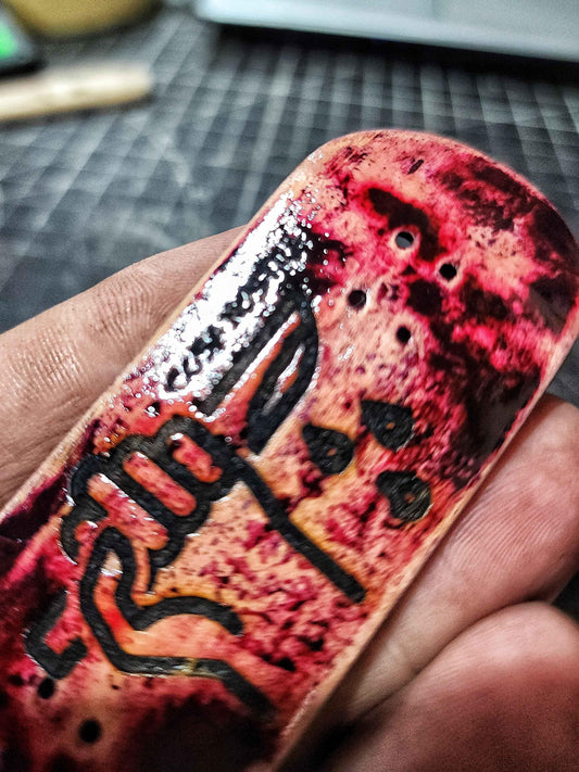 Hand holding a custom handmade fingerboard deck with red splatter art and black graphics.