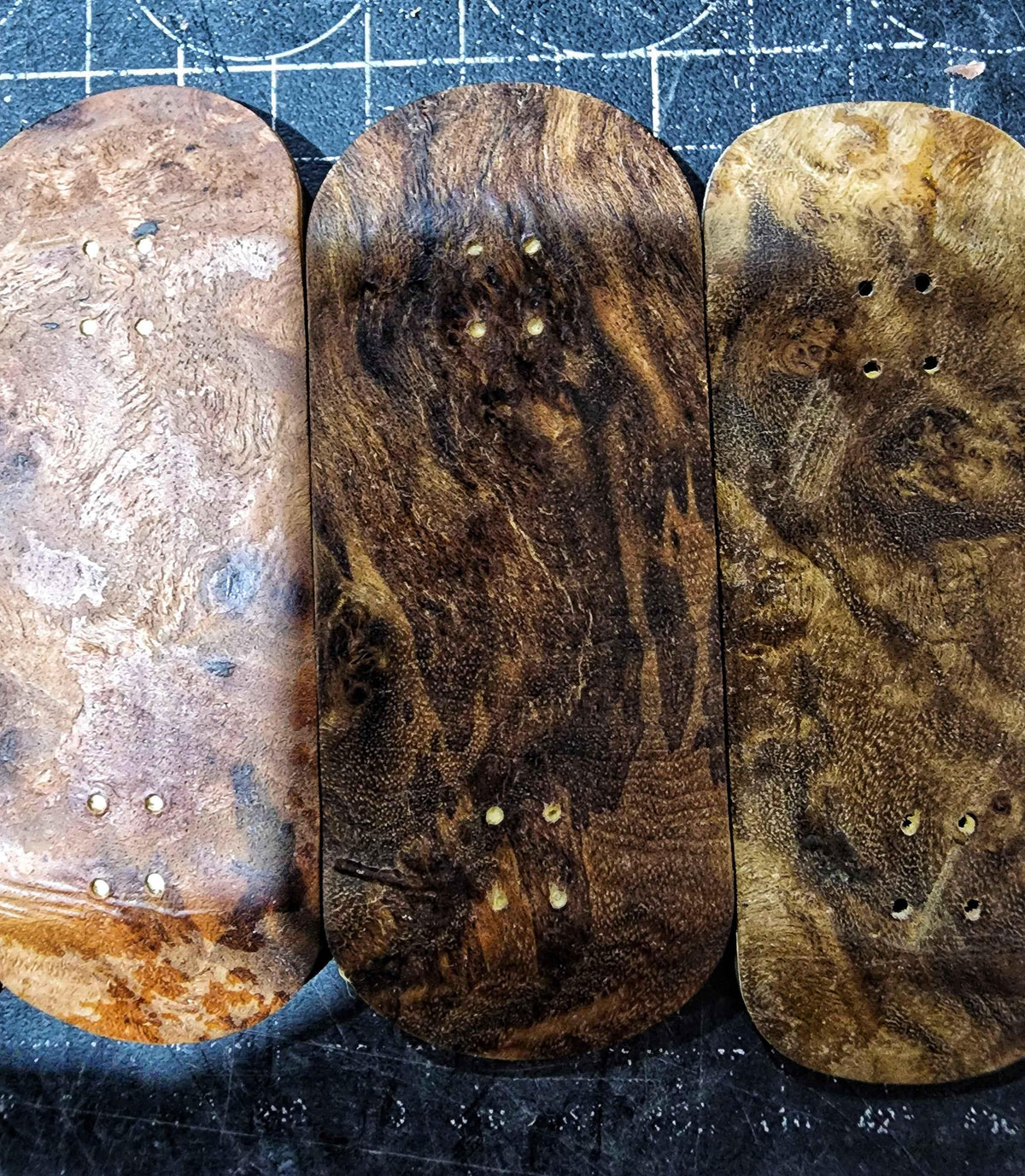 Three handmade custom wooden fingerboard decks with unique natural grain patterns.