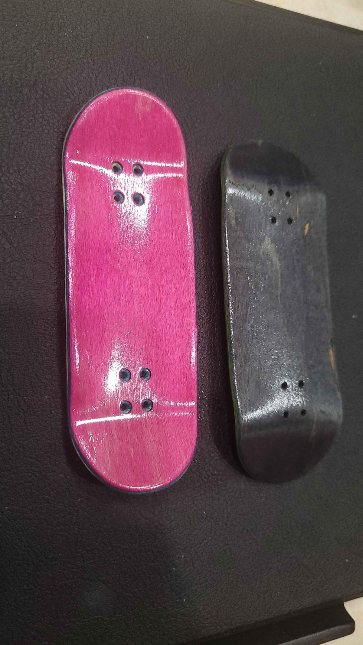 Two custom handmade fingerboard decks, one pink and one black, on a dark surface.