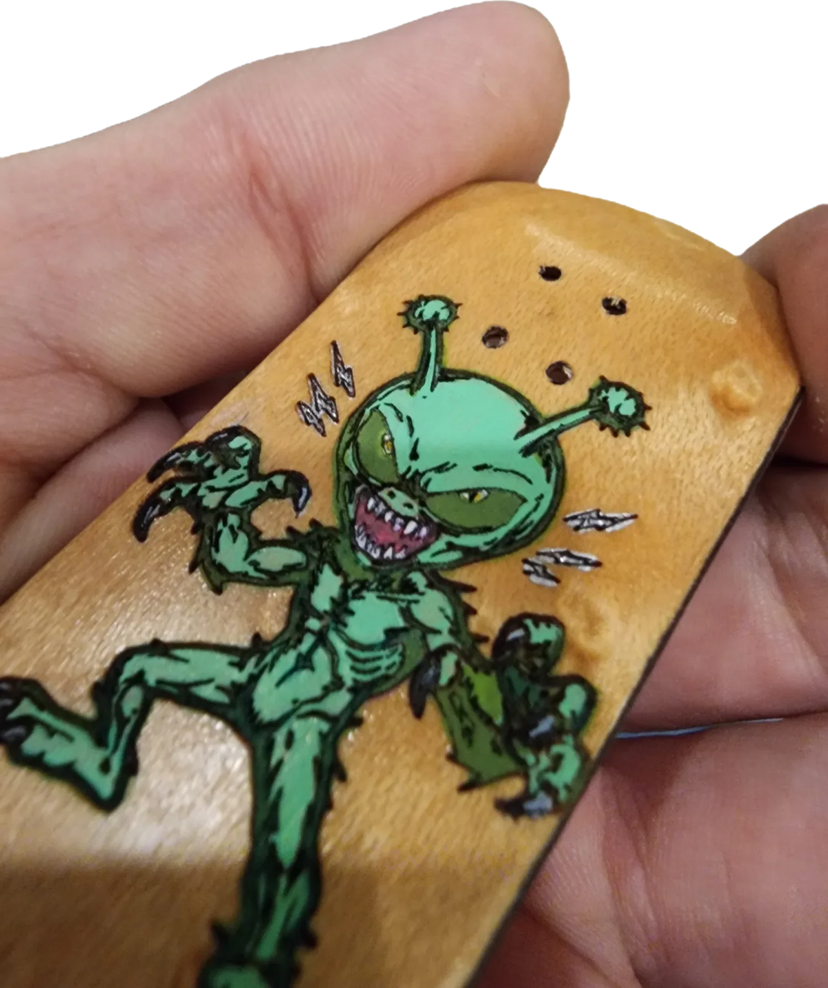 Close-up of a wooden fingerboard deck featuring a green alien monster graphic.
