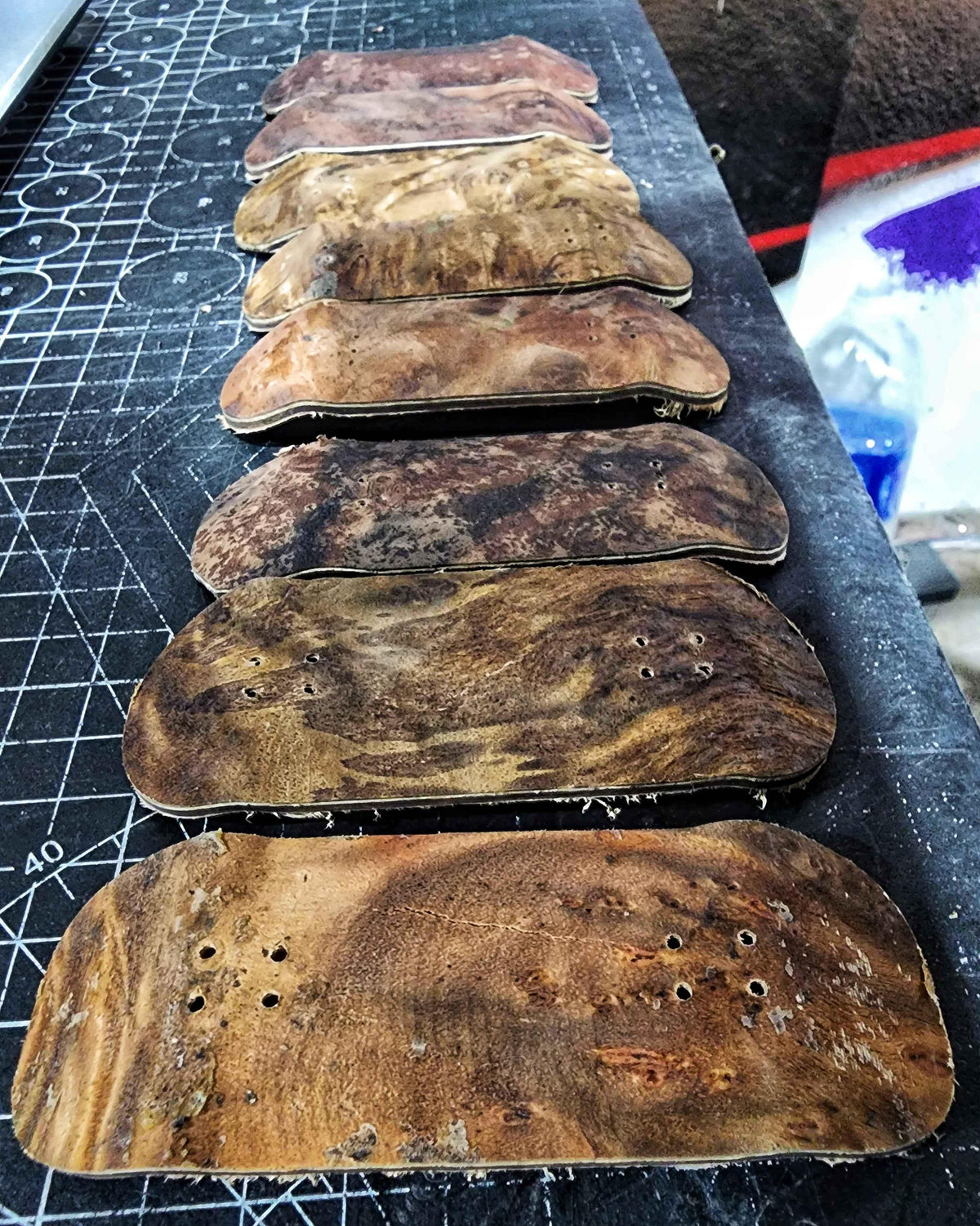 Row of handmade custom fingerboard decks with wood grain patterns on a cutting mat.