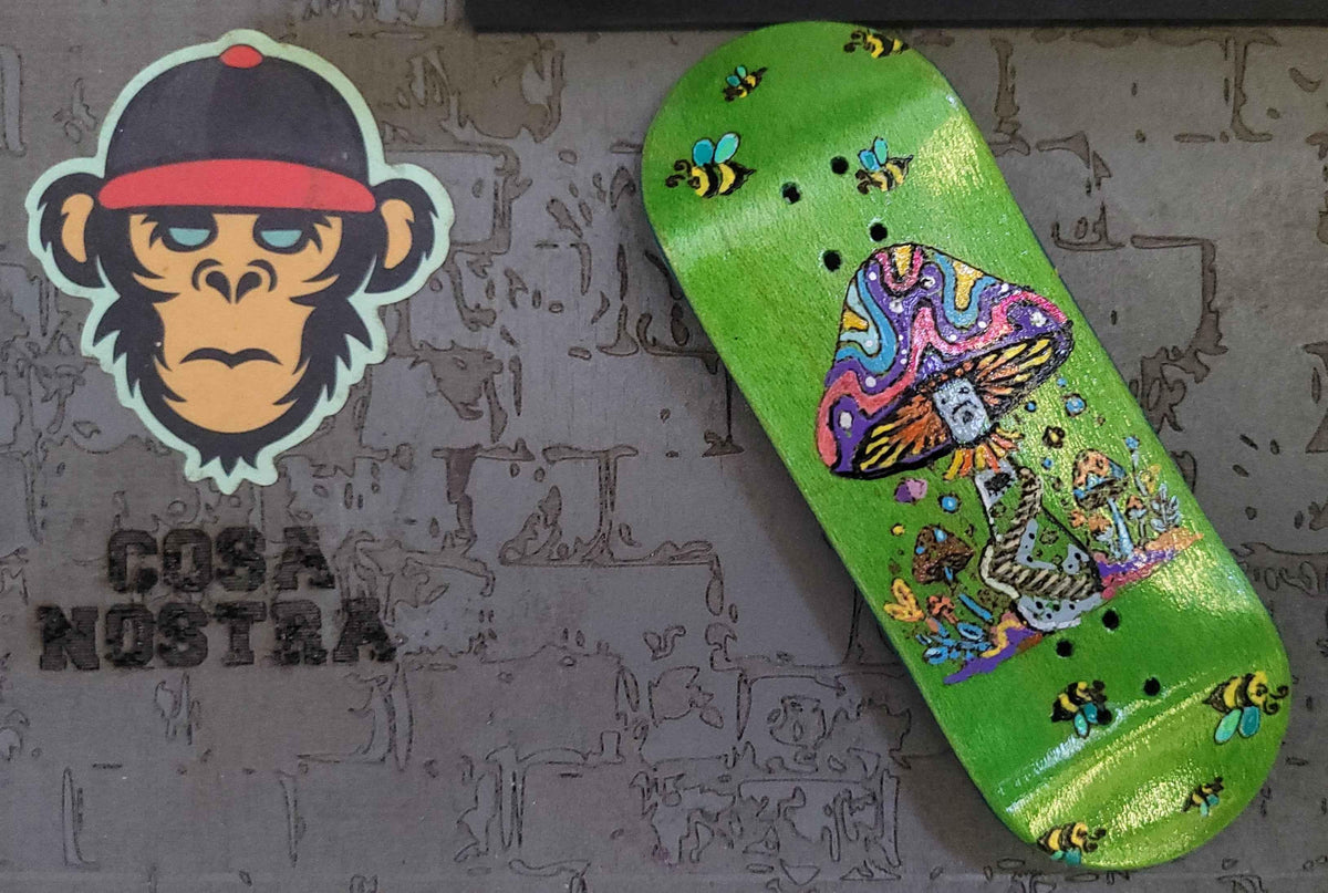Custom green fingerboard deck with psychedelic mushroom and bee artwork next to a monkey sticker