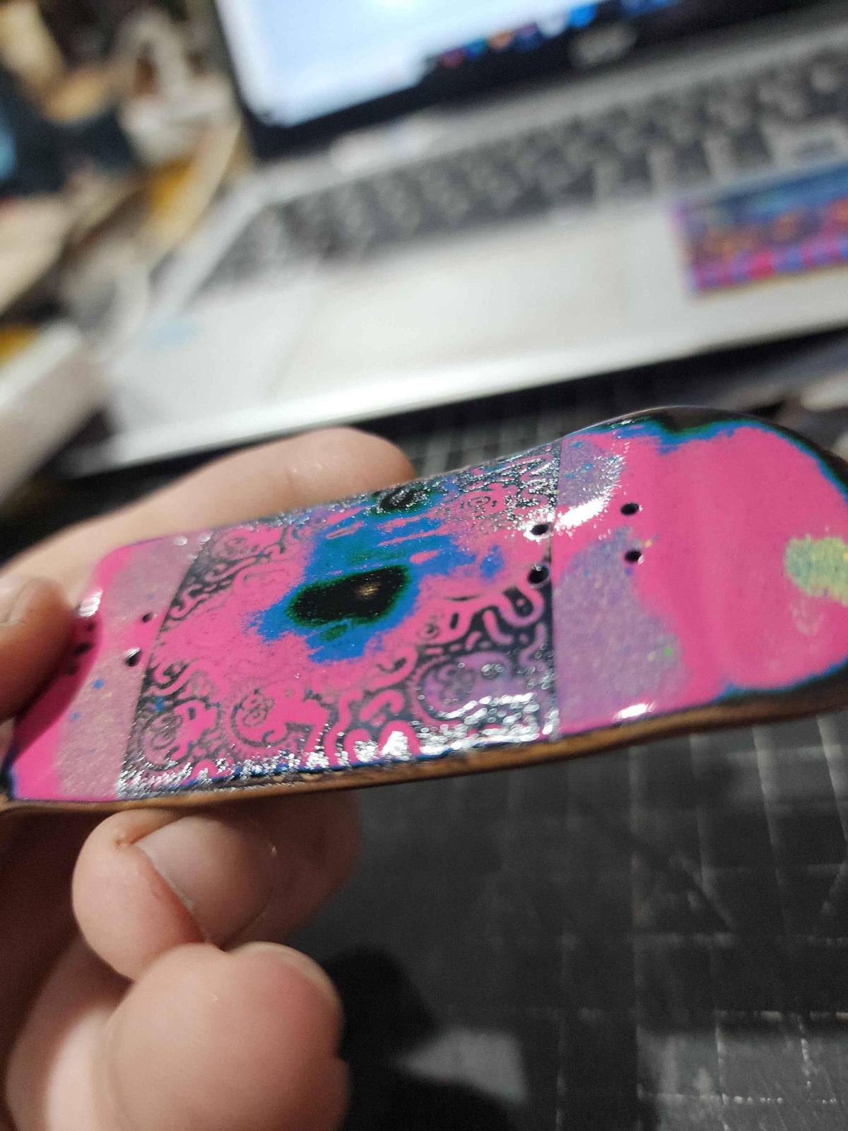 Close-up of a handmade custom fingerboard deck with colorful pink and blue abstract art.