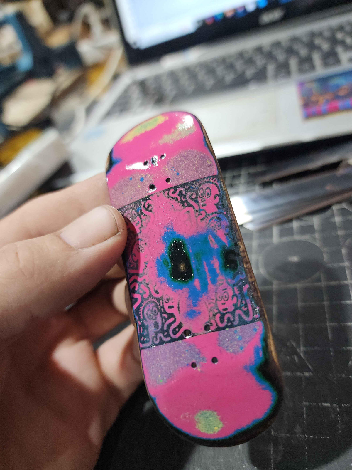 Close-up of a custom handmade fingerboard deck with pink and blue psychedelic graphics.