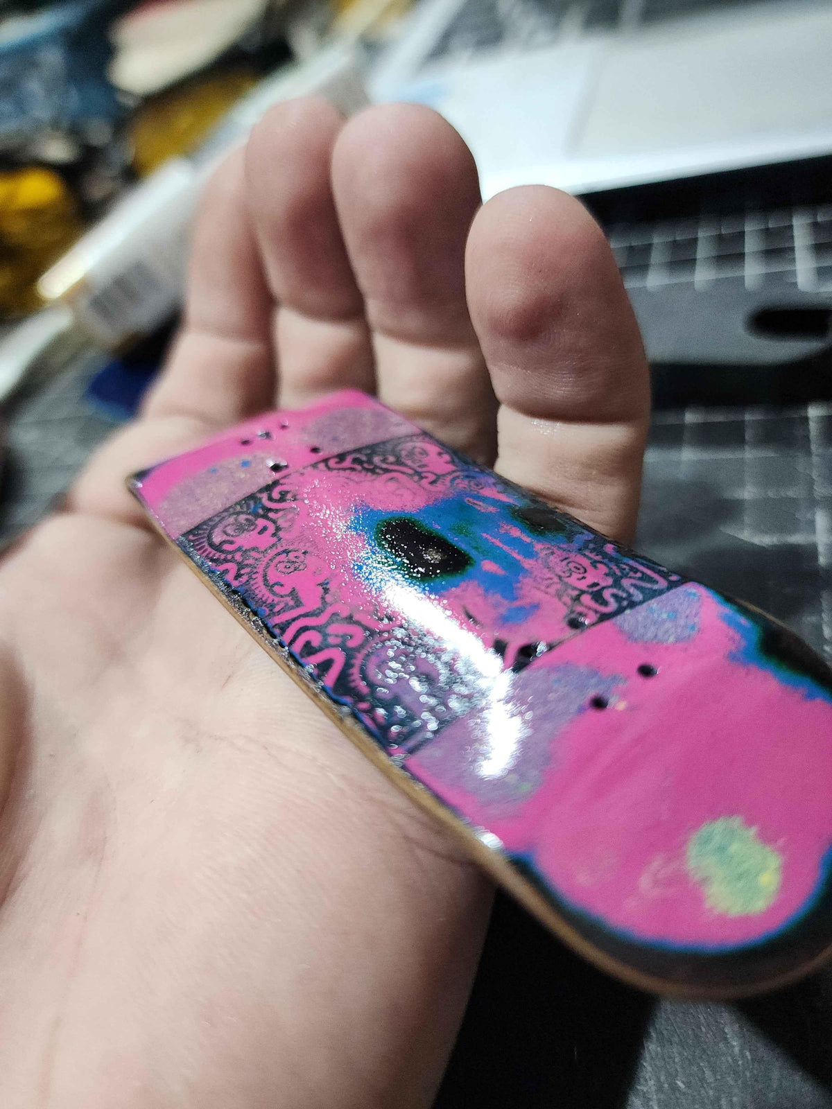 Hand holding a custom handmade pink and blue graphic fingerboard deck.