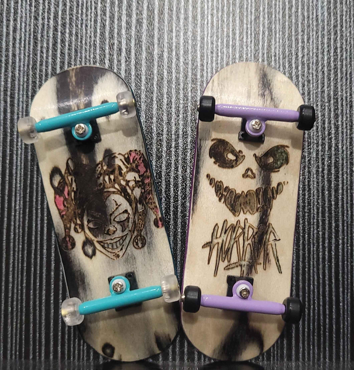 Two custom handmade fingerboard decks with graphic art and miniature trucks.