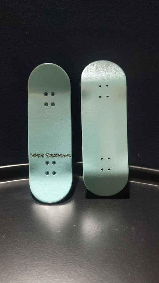 Two light teal handmade custom fingerboard decks on a dark surface.