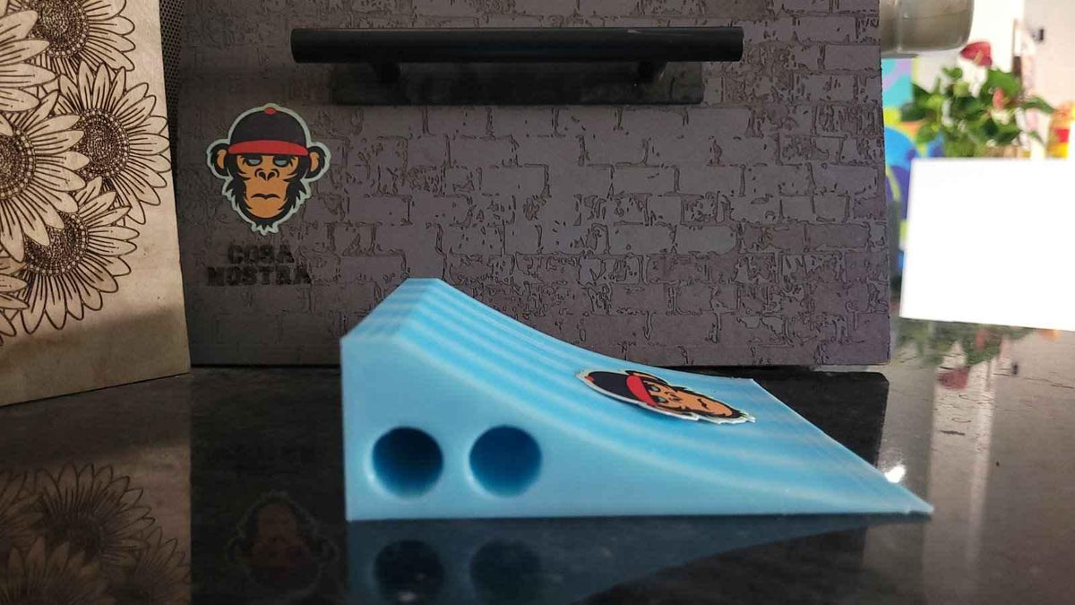 Light blue 3D printed fingerboard ramp with logo on a dark reflective surface.