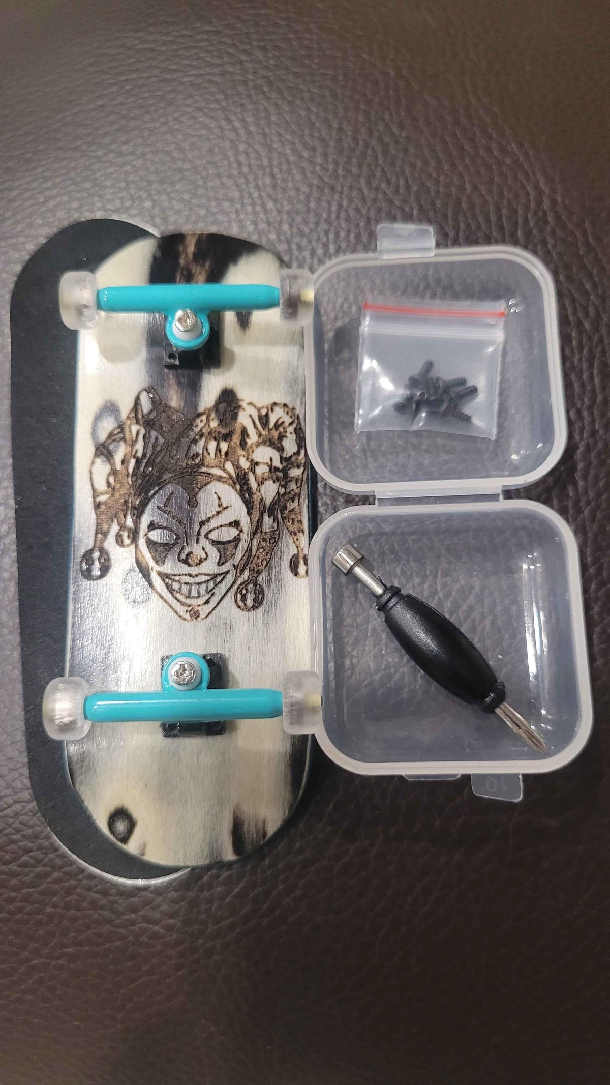 Custom fingerboard deck with jester graphic, mini trucks, wheels, screwdriver, and hardware kit.