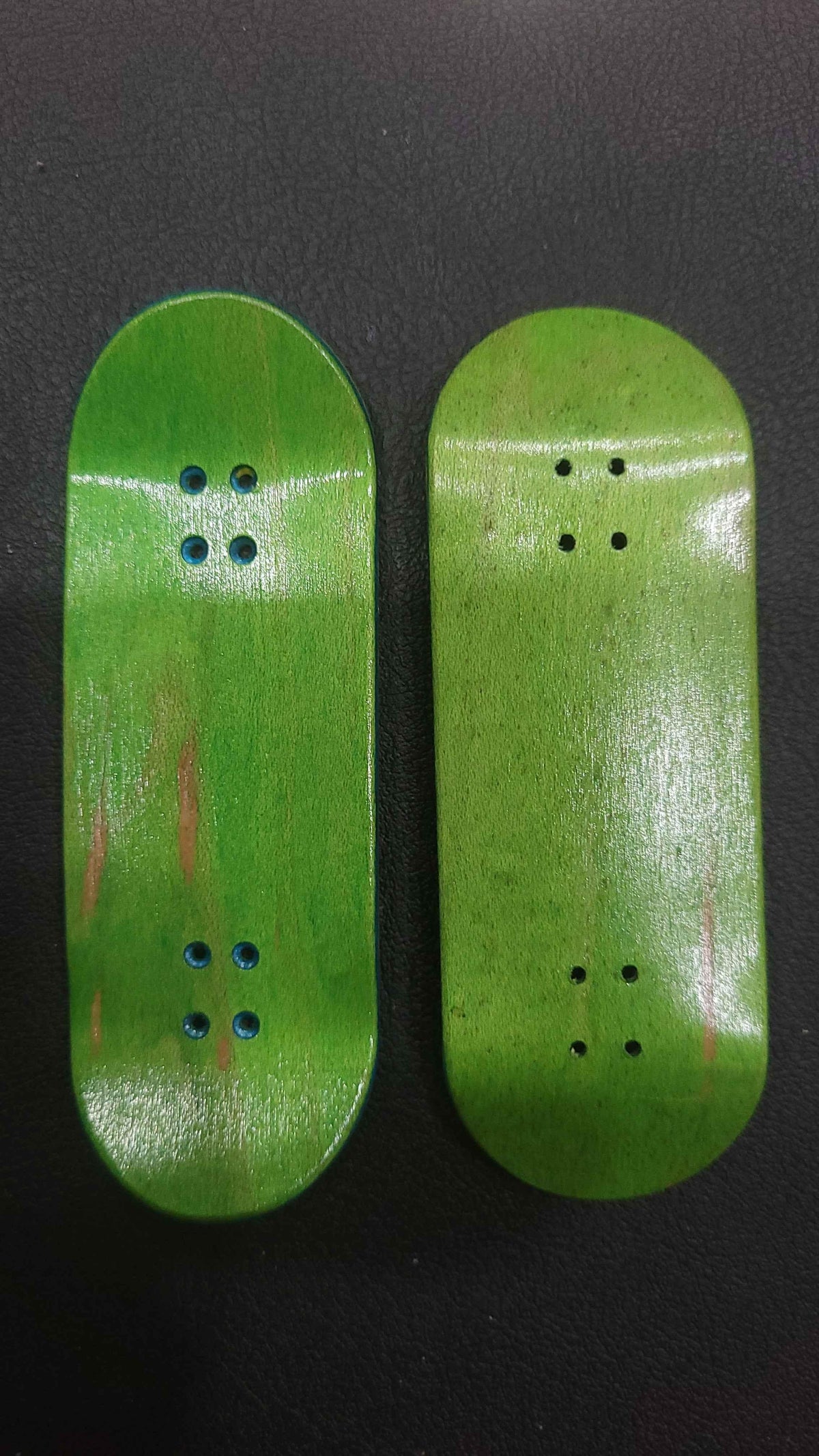 Two handmade green wooden fingerboard decks on a dark surface.