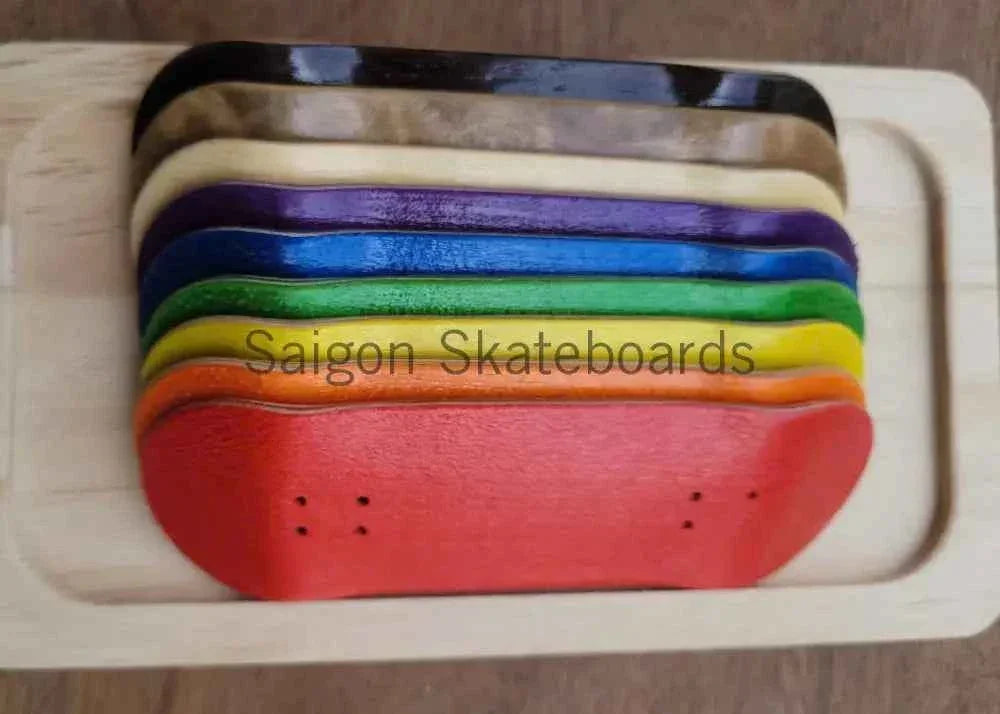 Stack of colorful handmade fingerboard decks in various vibrant colors on a wooden tray.