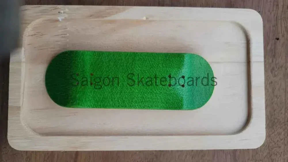 Green grip tape with 'Saigon Skateboards' text on a light wood fingerboard deck.