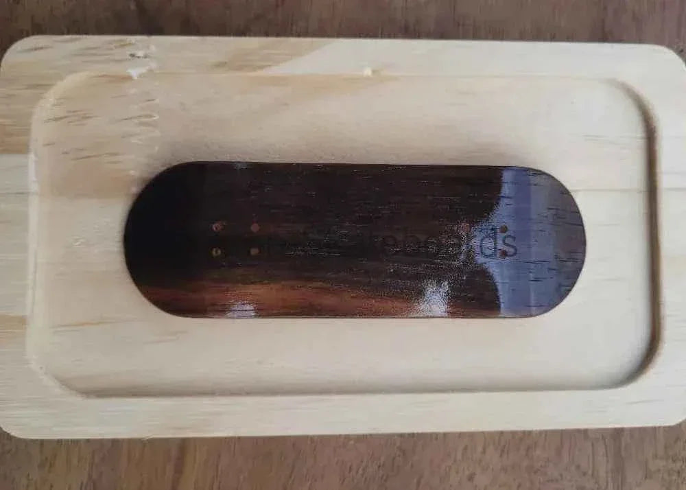 Handmade wooden fingerboard deck resting in a light wood display tray