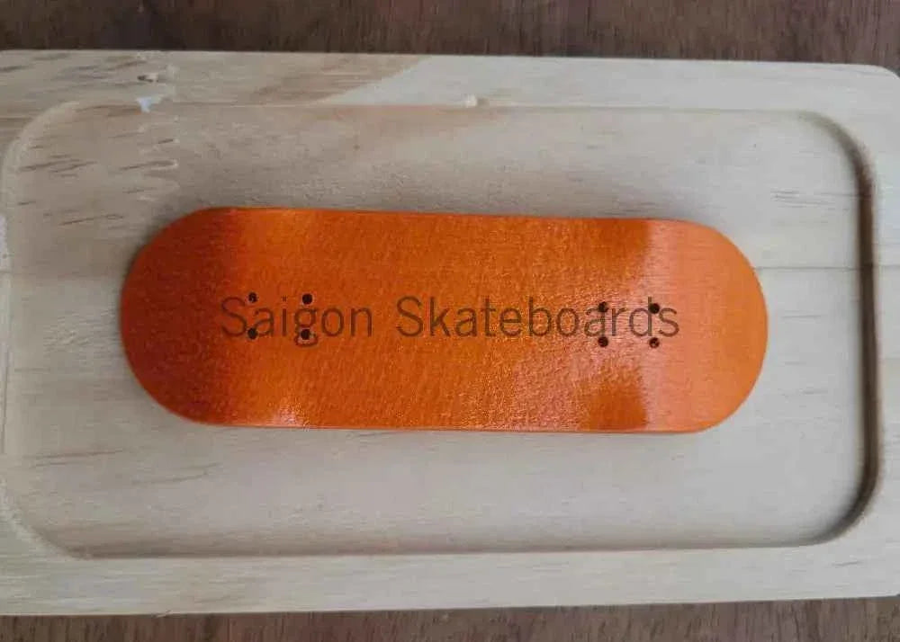 Orange custom fingerboard deck with 'Saigon Skateboards' text in a wooden display case