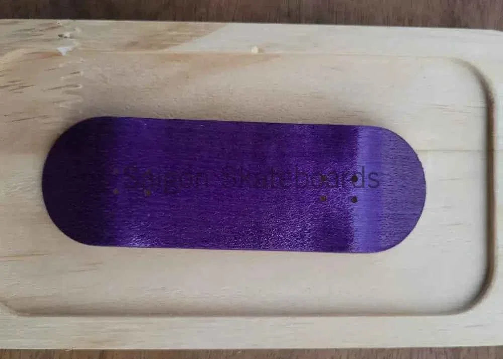 A purple grip tape sheet for fingerboards resting on a light-colored wooden deck.