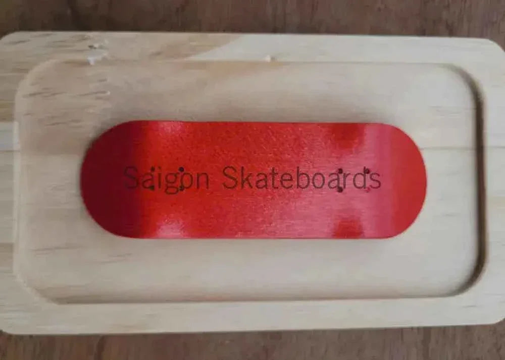 A red custom fingerboard deck resting in a wooden display tray with Saigon Skateboards text.
