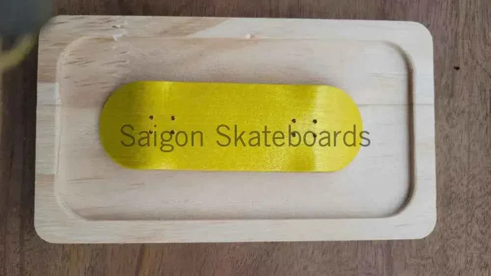 A gold fingerboard deck resting on a light wooden display tray with Saigon Skateboards text.