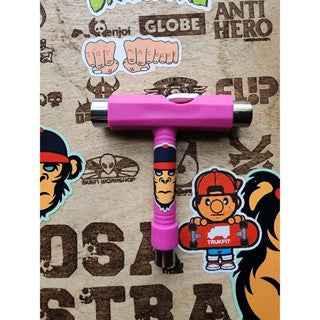 Pink fingerboard tool resting on a surface covered in various skate brand stickers.