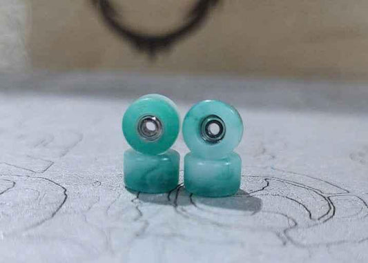 Two light turquoise custom fingerboard wheels with silver bearings.