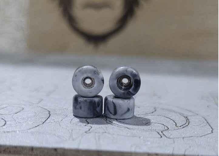 Four grey marbled fingerboard wheels resting on a textured surface