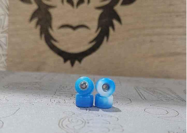 Two blue and white marbled fingerboard wheels on a textured surface