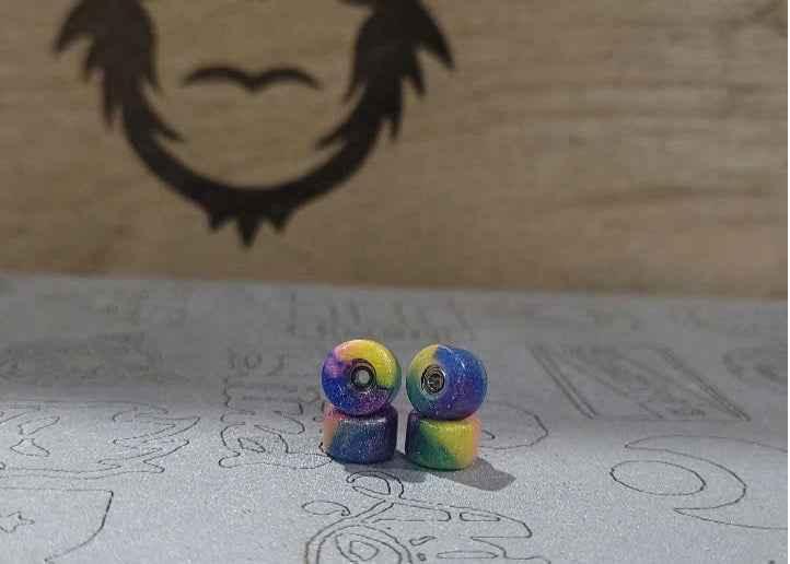 Two colorful, marbled fingerboard wheels with a blue, yellow, and purple gradient.