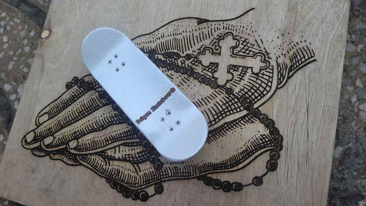 Saigon Skateboards white custom fingerboard deck on a wooden graphic background.