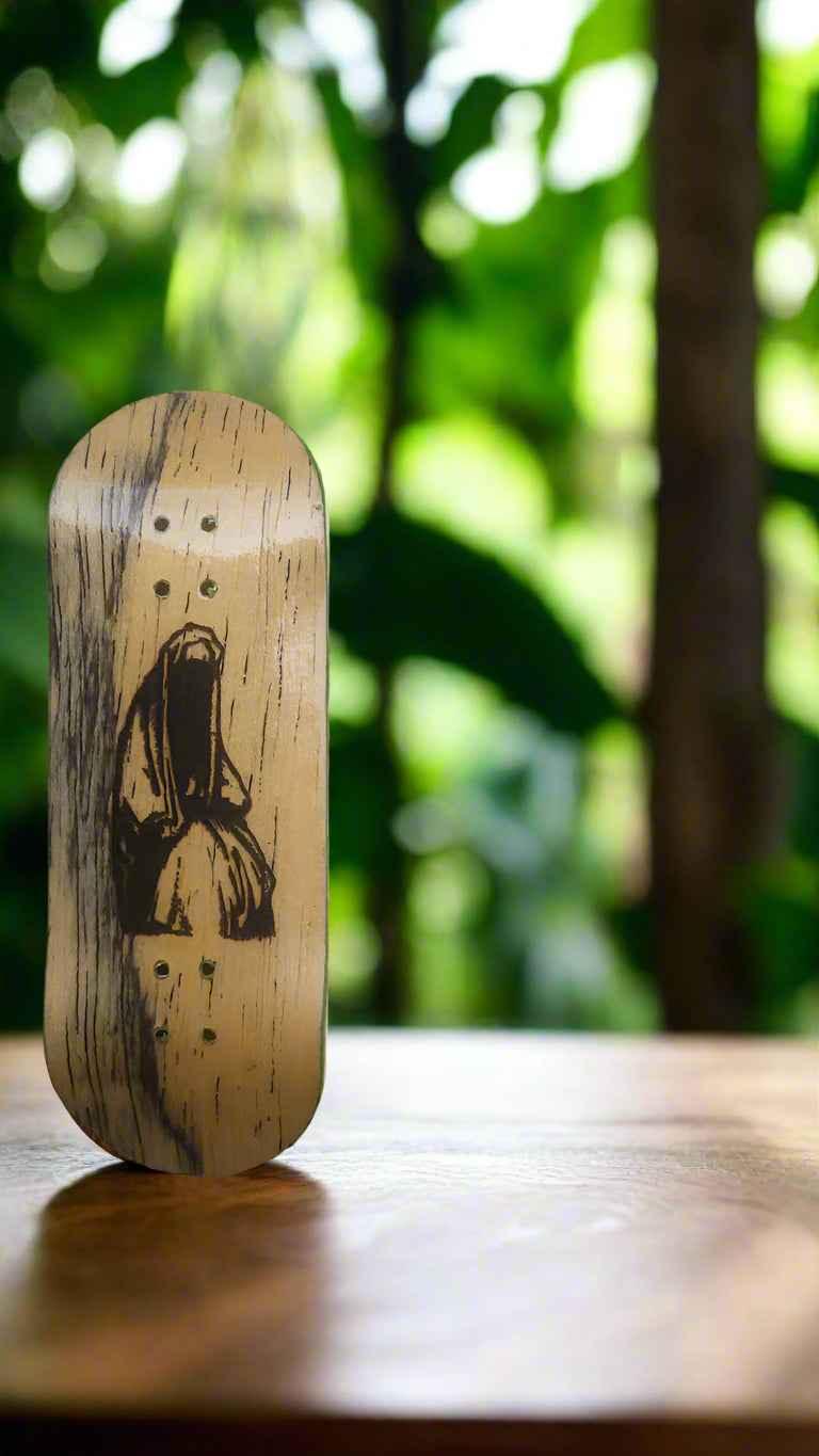 Handmade wooden fingerboard deck with a black artistic figure print on a wooden surface.