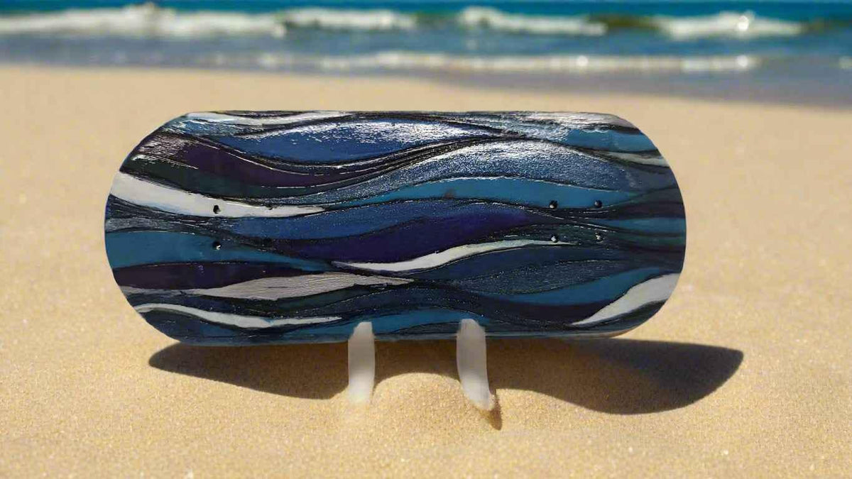 Custom handmade fingerboard deck with blue wave patterns on a sandy beach