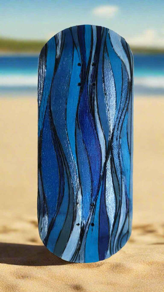 Handmade custom fingerboard deck with blue and grey abstract swirl design on a sandy beach.