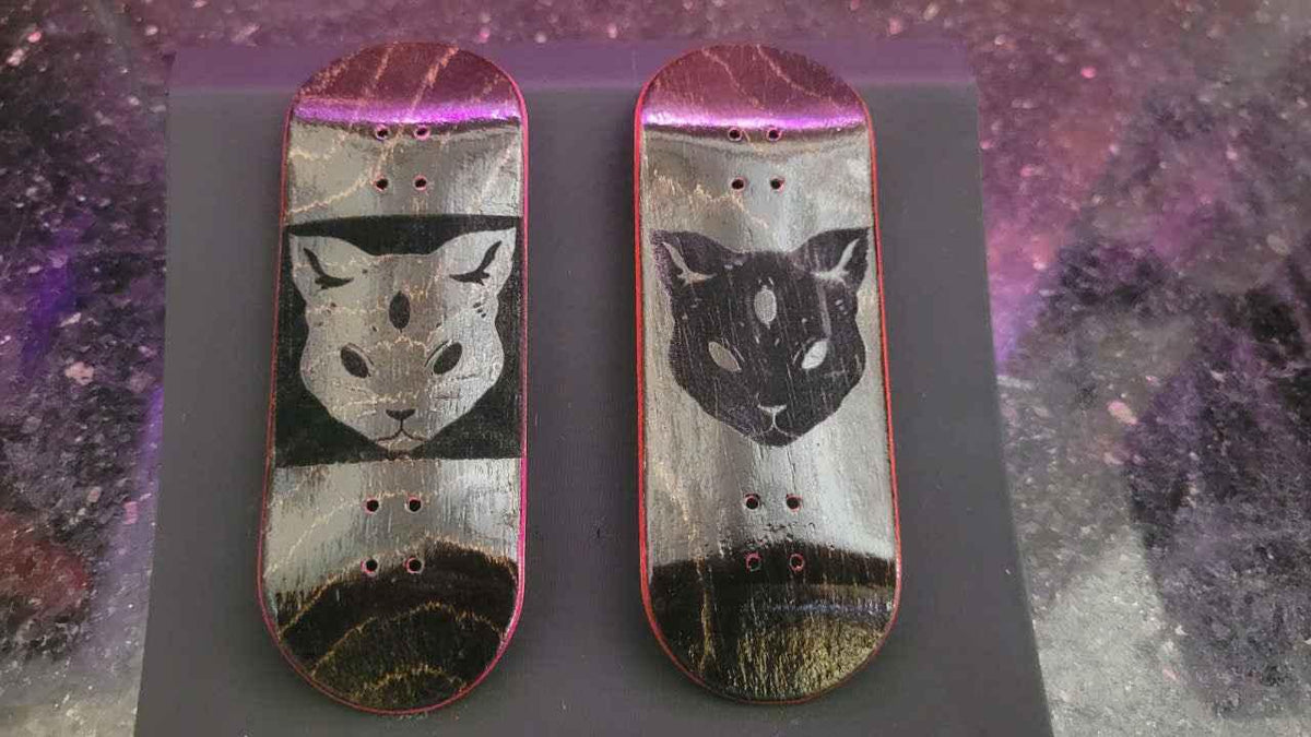 Two custom handmade fingerboard decks featuring cat face graphics and marbled finishes.