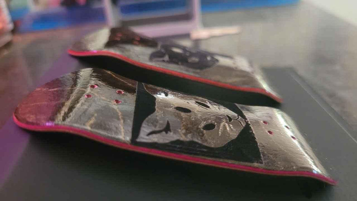 Two custom fingerboard decks with graphic designs and pink edges on a dark surface.