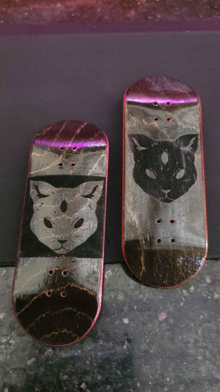 Two custom handmade fingerboard decks featuring black cat graphic designs