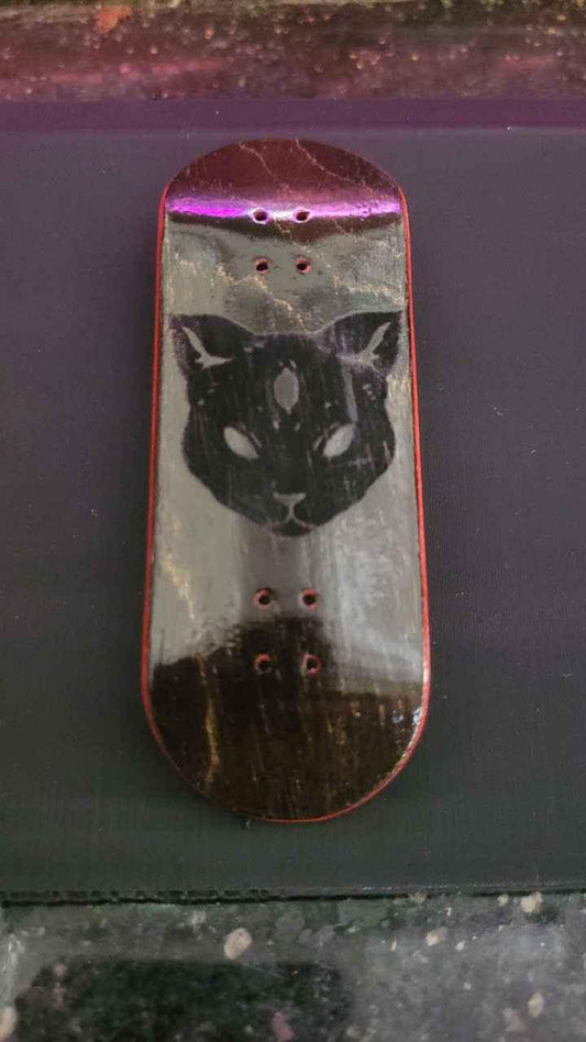 Custom fingerboard deck with a black cat face graphic on a dark wood finish